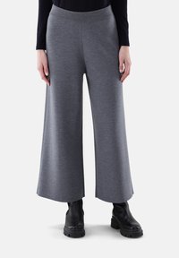 Graue weitgeschnittene Hose aus weichem Stoff, mit hohem Bund und glatter Textur. Getragen mit schwarzen Ankle Boots.