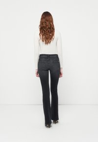 Sorte vide jeans med høy midje, med stikrede baklommer og en myk denimtekstur. Kombinert med en tettsittende hvit topp.