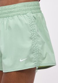 Ανοιχτό πράσινο αθλητικό σορτς με ελαστική μέση, πλαϊνό φερμουάρ και μικρό λευκό σήμα Nike στο αριστερό πόδι.
