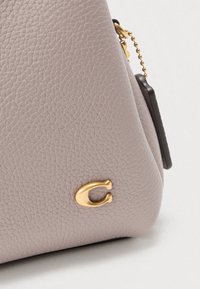 Sac à main en cuir violet texturé avec un détail logo doré, présentant une forme structurée et un petit détail chaîne attaché.