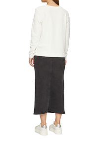 Un haut blanc texturé à manches longues associé à une jupe midi en denim noir et des baskets blanches volumineuses avec des accents argentés, vu de dos.