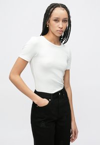 Biały prążkowany top z krótkim rękawem zestawiony z wysokim stanem czarnych dżinsów ozdobionych subtelnymi haftowanymi wzorami i przednimi kieszeniami.