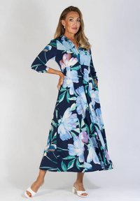 Kwiatowa sukienka midi w kolorze granatowym, z dużymi jasnoniebieskimi i fioletowymi kwiatami. Długie rękawy, zapięcie na guziki z przodu i luźny krój.