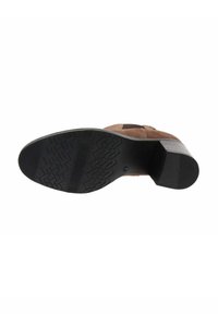 Botte en suède marron vue du dessous, montrant une semelle texturée noire et un talon empilé sur un fond blanc.