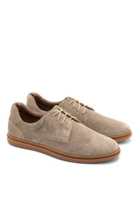 Zapatos de gamuza beige con un diseño perforado, punta redonda y cordones finos. Cuentan con una suela de goma marrón y una estructura casual y ligera.