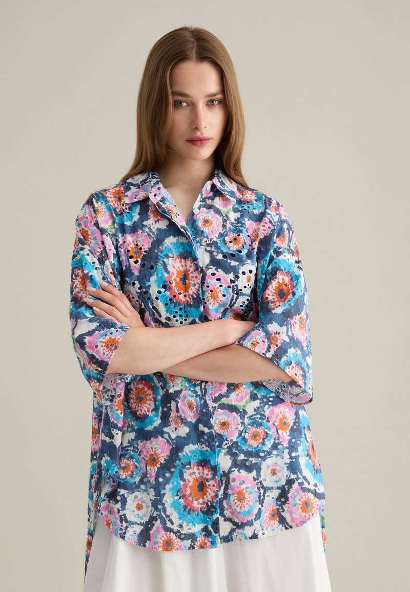 Camicia a maniche corte con bottoni, con un motivo floreale dai colori vivaci di blu, rosa e arancio, dal fit rilassato. Tessuto leggero.