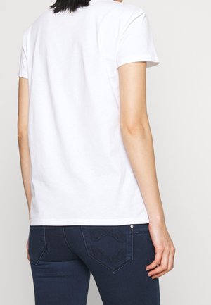 Camiseta de algodón blanca de manga corta, con cuello redondo. Se lleva con vaqueros azul oscuro que tienen bolsillos traseros bordados.