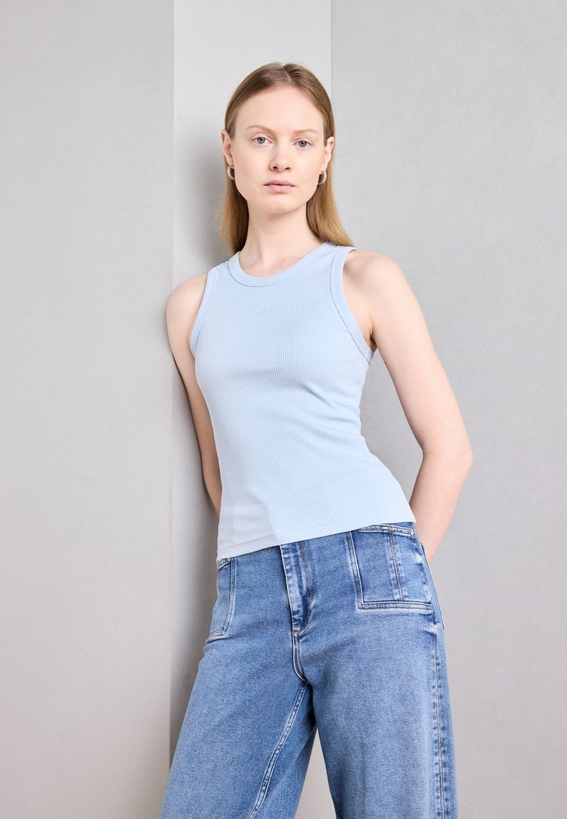 Lys blå ribbet tanktop med rund hals, kombinert med høyt liv lys blå denim bukser. Enkel, tettsittende design uten dekorasjoner.