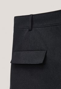 Gros plan d’un pantalon en tissu noir montrant la ceinture avec passants pour ceinture et une poche à rabat.