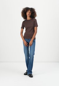 Braun gestreiftes T-Shirt mit kurzen Ärmeln aus Baumwolle, kombiniert mit blauen Jeans. Auffällige Akzente sind ein kleines Logo auf der Brust.