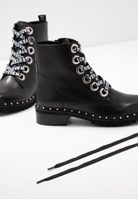 Bottines en cuir noir avec œillets en métal argenté, lacets décoratifs et clous le long de la semelle. Comprend des lacets noirs.