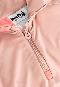 Hellrosa Zip-Jacke mit einem sternförmigen Reißverschluss, glatter Textur und kontrastierenden korallenfarbenen Akzenten. Das Etikett trägt die Aufschrift "WeeDo Funwear."