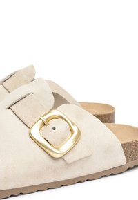 Sandales en suède beige avec une large sangle ornée d'une boucle carrée en or, semelle en liège et semelle en caoutchouc texturé pour plus d'adhérence.