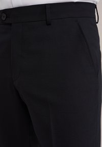 Svarta byxor i ett strukturerat tyg, med rak skärning, sidofickor och knäppning vid midjan.