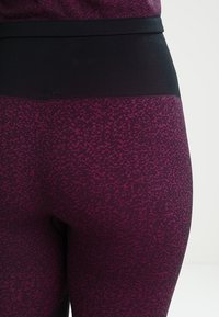 Leggings con un tejido texturizado de color púrpura oscuro y una cinturilla elástica negra, diseñados para ofrecer comodidad y flexibilidad.