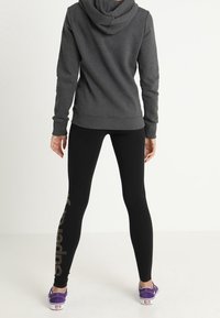 Felpa grigia scura con una vestibilità aderente, abbinata a leggings neri con un design testuale verticale glitterato e scarpe da ginnastica viola.