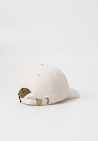 Beige baseball cap with a curved brim, made of cotton, featuring a brass buckle at the back and visible stitching details.