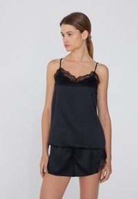 Ensemble de cami et shorts en satin noir avec dentelle le long des bords. Bretelles spaghetti réglables, coupe décontractée et texture lisse.