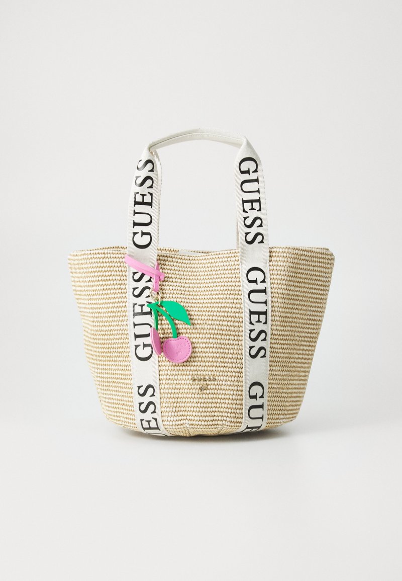 Woven straw tote bag with white "GUESS" logo straps, featuring a pink and green cherry charm attached for a decorative detail.