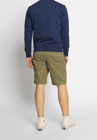 Marinblå sweatshirt, olivgröna shorts och beige hög-top sneakers. Sweatshirten har långa ärmar; shorts är knälånga med fickor.