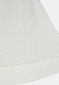 Tecido branco texturizado com um padrão ondulado, com um acabamento suave na bainha e detalhes de costura sutis ao longo da borda inferior.