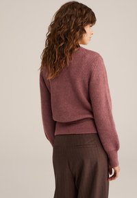 Pletena mauve džemper s rebrastom teksturom, okruglim izrezom i blago skraćenim krojem, uparen s smeškim hlačama s prugama.