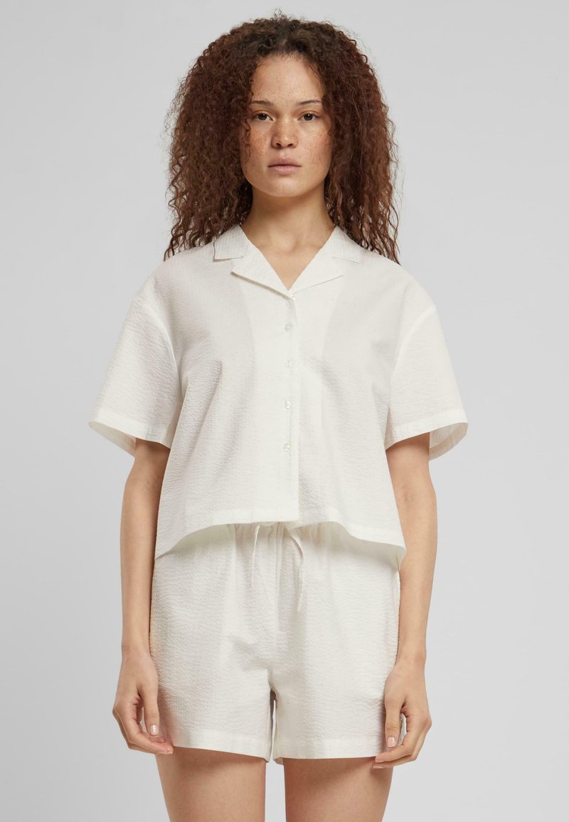 Kortermet, krageformet hvit skjorte med teksturert stoff, knapplukking, kombinert med matchende shorts med elastisk midje.