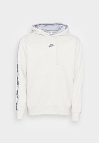 Vit hoodie med framficka, grå dragsko och grå Nike-logotyp. Har mönstrade ärmdekorationer med svart och grå design.