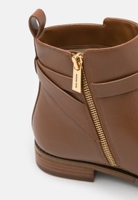 Bottine en cuir marron avec fermeture éclair dorée et languette, dotée d'un petit talon en bois et d'un tire-zip de marque.