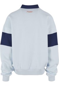 Lyseblå genser med marineblå striper på ermene. Har ribbestrikkede mansjetter og krage. Brodert "Forbudt" på baksiden av halslinjen.