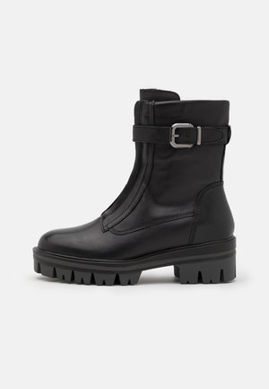 Botte mi-mollet en cuir noir avec semelle à crampons épaisse, bride latérale à boucle et finition lisse, vue de profil sur un fond uni.