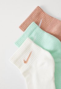 Three pairs of socks: white with orange logo, mint green, and light pink, all with ribbed texture and contrasting logo accents.