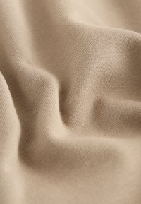 Tissu en maille beige clair avec une surface douce et texturée, présentant une subtile élasticité et un drapé fluide qui crée de douces ondulations.