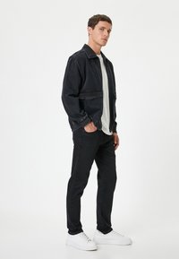 Chaqueta de mezclilla negra con cuello ancho, dos bolsillos frontales; combinada con pantalones ajustados negros y zapatillas blancas. Diseño simple y sin costuras.
