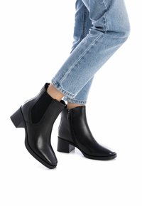 Stivaletti neri in pelle con pannelli laterali elastici e una zip decorativa, caratterizzati da una punta quadrata e un tacco a blocco.