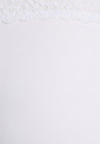 Fehér anyag, sima, rugalmas textúrával, a tetején csipkés, hullámos szegéllyel, amely egy finom részletet ad hozzá.