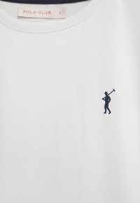 Wit Polo Club-shirt met een klein marineblauw geborduurd polo-spelerlogo op de borst en een maatlabel "S" aan de binnenkant van de kraag.