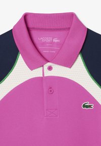 Slim fit polo med en rosa front och kortärmar i marinblått. Inkluderar en grön krage accent och en perforerad vit panel. Lacoste-logotyp.