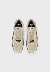 Ténis Nike SB com parte superior em malha bege, detalhes em preto e um design texturizado. Inclui atacadores e um colarinho almofadado.