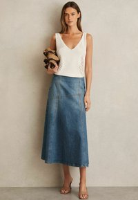 Crème gebreide top met een V-hals en opengewerkte details, gecombineerd met een lange denimrok met zichtbare stiksels en zijnaad.