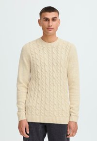 Pulover cu tricotaj cabluri în bej deschis, cu gât rotund, mâneci lungi și manșete și tiv dintr-un material încrețit. Model texturat pe întreaga suprafață.