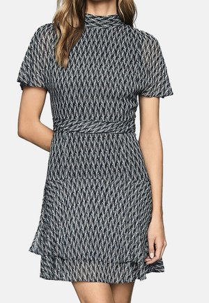 Kobieta ubrana w czarno-białą sukienkę z krótkim rękawem, z wysokim dekoltem i falbanową spódnicą.