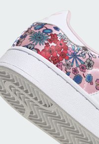 Valge kummist tallaga toss, mille peal on roosa lillemustriga ülaosa. Disainil on erksavärvilised sinised ja punased lillid läikivate detailidega.