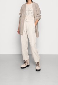 Cárdigan beige acanalado, camiseta gráfica crema, pantalones plisados beige claro y botas militares crema con suelas y cordones negros.