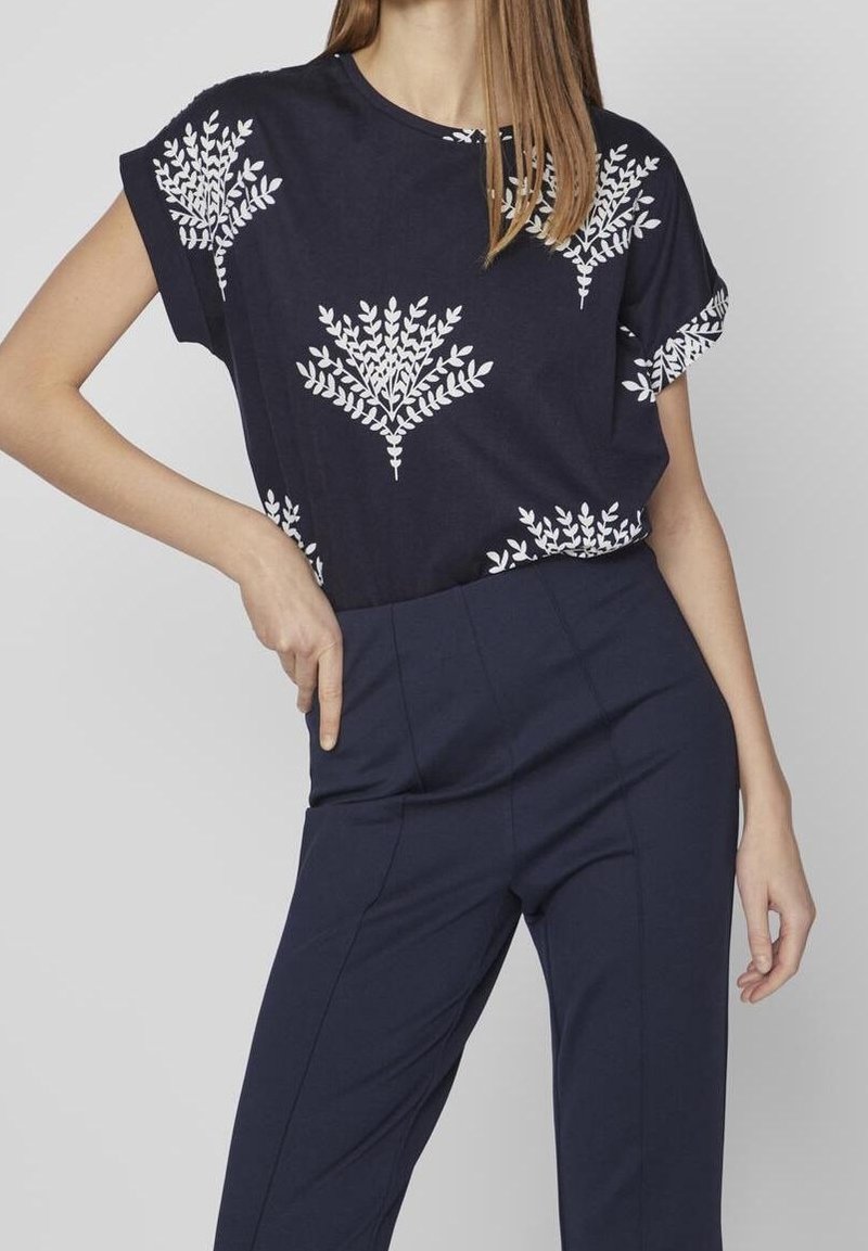 Námořnická modrá krátká rukávová blůza z bavlny, která se vyznačuje bílým vzorem listů. Spárována s námořnickými kalhotami, zdůrazňující uvolněný střih a měkkou texturu.