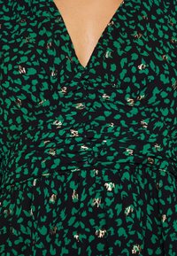 Grön och svart klänning med djup V-halsringning, rynkad bodice och guld djurmönstrade detaljer på en texturerad tyg.