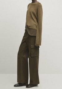 Pull marron texturé à manches longues, associé à un pantalon cargo à jambes larges avec poches latérales. Tenue aux tons terreux au design épuré.