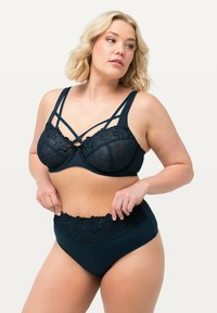 Donkerblauwe bh met doorschijnende bloemenkant cups en kruislings straps; bijpassende high-waisted slip met een kanten tailleband.