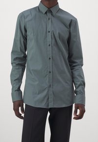 Camicia verde scuro a maniche lunghe con bottoni, realizzata in tessuto liscio con colletto classico e bottoni tono su tono, caratterizzata da una silhouette aderente.
