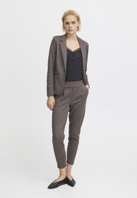 Checked blazer and pants set in brown and black with a fitted design. Sleeveless black top with lace neckline, worn with flat black shoes.